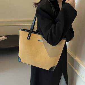 Detail of a large yellow suede tote bag with black leather straps and silver metal logo