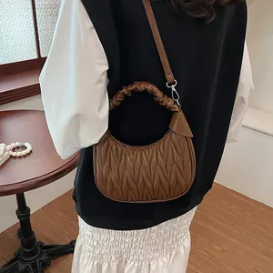 Close-up of brown pleated half-moon bag featuring a ruffled handle and detachable strap