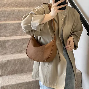 Sac demi-lune en cuir plissé marron porté à l'épaule devant un décor d'escalier