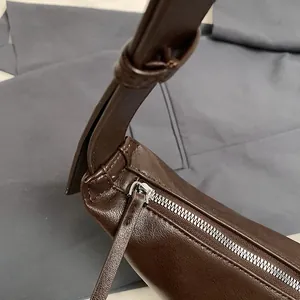 Detalle del cierre de cremallera plateado y costuras en el bolso de cuero marrón