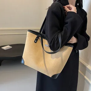 Detail of beige suede tote bag with black leather trim worn on shoulder with wool coat