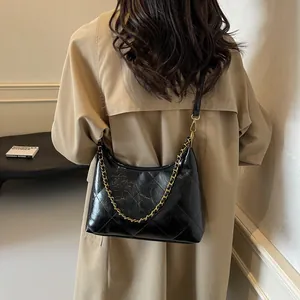 Detail of black quilted shoulder bag with gold chain strap on a trench coat model
