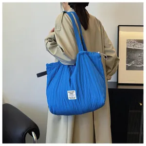 Detail of blue pleated nylon tote bag with brand label worn by model in beige coat