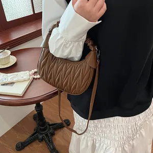 Close-up of brown pleated half-moon handbag with matelassé quilting and crossbody strap