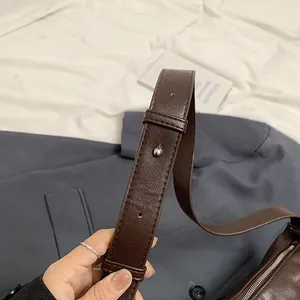 Detalle de bolso de cuero marrón oscuro con hebilla ajustable plateada y textura fina