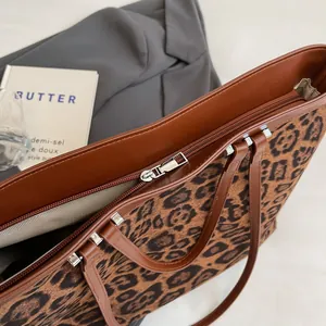 Close-up of leopard print tote bag with brown leather handles and metal zipper detail