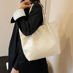 Minimalist beige tote bag in soft leather texture worn on shoulder over black blazer