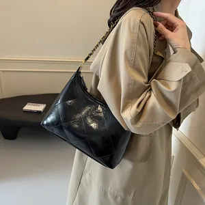 Detail of black quilted shoulder bag featuring glossy patent leather and a metal chain strap