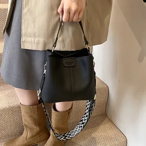 Detail of black pebbled bucket bag with geometric ethnic shoulder strap on indoor stairs