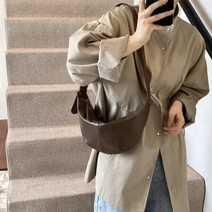 Primer plano de un bolso de media luna marrón oscuro en cuero mate con costura decorativa