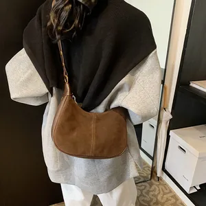 Détail d'un sac hobo en daim marron avec garniture en cuir et boucle dorée à l'épaule