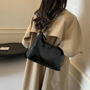 Model wearing a black quilted leather bag with a gold chain strap over a khaki trench coat