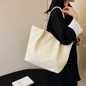 Side view of an oversized cream leather tote bag with slim handles for daily commute