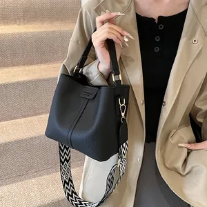 Detail view of black bucket bag with lychee texture and geometric patterned strap