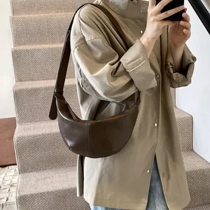 Detalle del bolso de media luna en cuero marrón oscuro con textura suave y correa ajustable