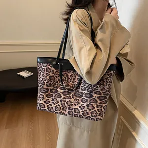 Detail view of large leopard print tote bag with black leather straps on a model