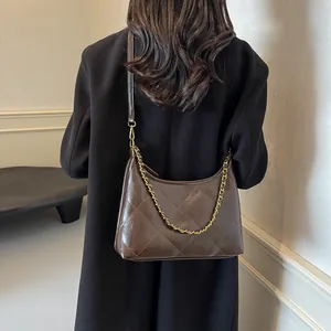Detail of dark brown quilted shoulder bag with gold chain strap worn over a black coat