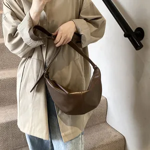 Bolso de media luna marrón con costuras verticales usado con una gabardina caqui