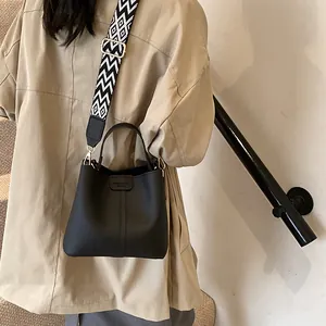 Black pebbled leather bucket bag with geometric wide strap shown on a model's shoulder