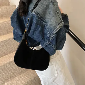Détail d'un sac demi-lune en daim noir avec boucles dorées porté à l'épaule sur jean