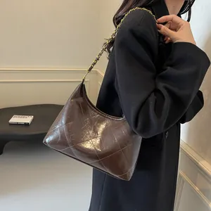 Detail of a brown quilted underarm bag with gold chain strap on a black coat outfit
