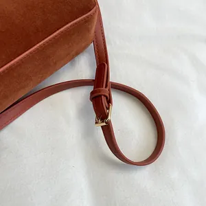 Détail du sac cabas en daim marron rouge avec bandoulière et boucle dorée élégante