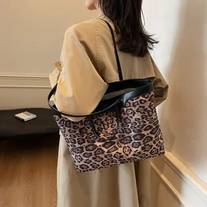 Detail of leopard print tote bag with black leather handles shown on shoulder