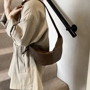 Detalle de bolso medialuna marrón oscuro con gabardina beige para un estilo retro chic