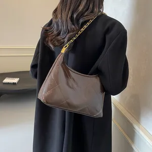 Detail view of glossy brown quilted shoulder bag with gold chain strap on model