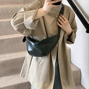 Detalle de un bolso de media luna oscuro con líneas acolchadas sobre una gabardina beige