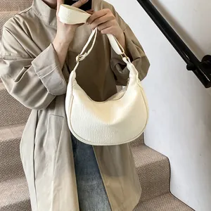 Sac sous le bras blanc en forme de croissant porté avec un trench beige style automne