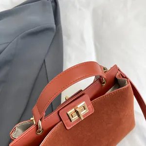 Détail d'un sac à main marron-rouge avec fermoir doré rotatif et textures contrastées