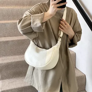 Gros plan d'un sac demi-lune blanc texturé litchi porté sur une chemise kaki