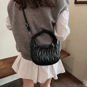 Detail view of black pleated crescent handbag featuring V-quilted texture and crossbody strap