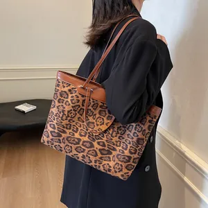 Large leopard print tote bag with brown leather straps shown on model in a minimalist room