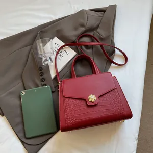 Detail of red crocodile texture tote bag with golden pearl buckle on a stylish desk