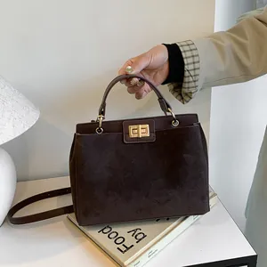 Gros plan du sac Kelly en daim marron foncé avec fermoir doré et poignée supérieure robuste