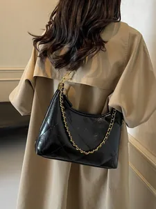 Quilted black leather underarm bag with gold chain strap worn with a beige trench coat