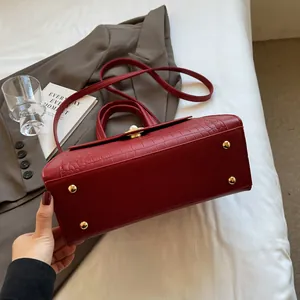 Detail view of red faux-leather handbag with crocodile pattern and golden protective studs