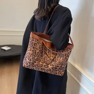 Detail of a large leopard print tote bag with brown leather trim styled on a model's shoulder