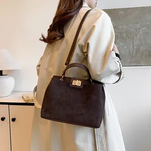 Détail d'un sac à main marron foncé mat avec fermoir doré porté sur un manteau beige