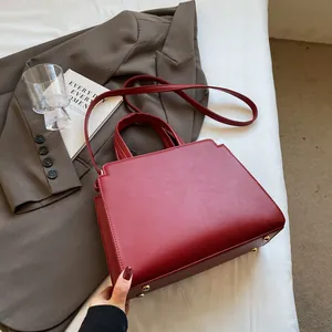 Close-up of wine red tote bag with gold protective base studs on a white sheet
