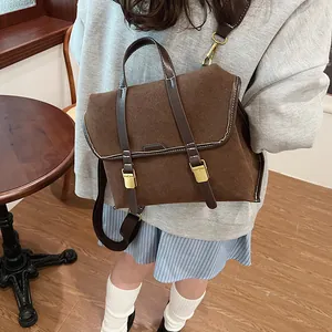 Detail of a brown matte backpack with leather straps and gold metal buckles on a model