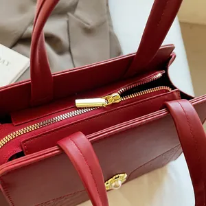 Detail of stone pattern texture, golden zipper, and pearl metal buckle on deep red tote bag
