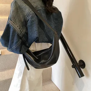 Detalle de un bolso de hombro negro de media luna minimalista usado por una modelo
