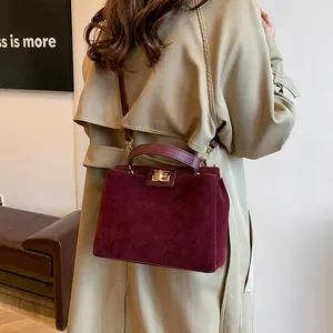 Détail d'un grand sac cabas bordeaux en daim avec fermoir doré sur un trench-coat
