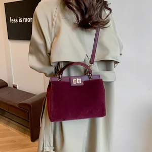 Détail du sac Kelly bordeaux en daim avec fermoir rotatif métallique sur trench-coat