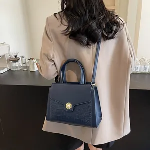 Detail of navy blue leather tote bag with crocodile pattern and pearl button on model