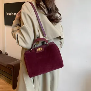 Modèle portant un sac cabas bordeaux en daim avec fermoir doré et bandoulière amovible