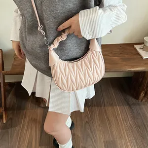 Detail of light pink pleated matelasse crescent bag worn by model in cozy interior